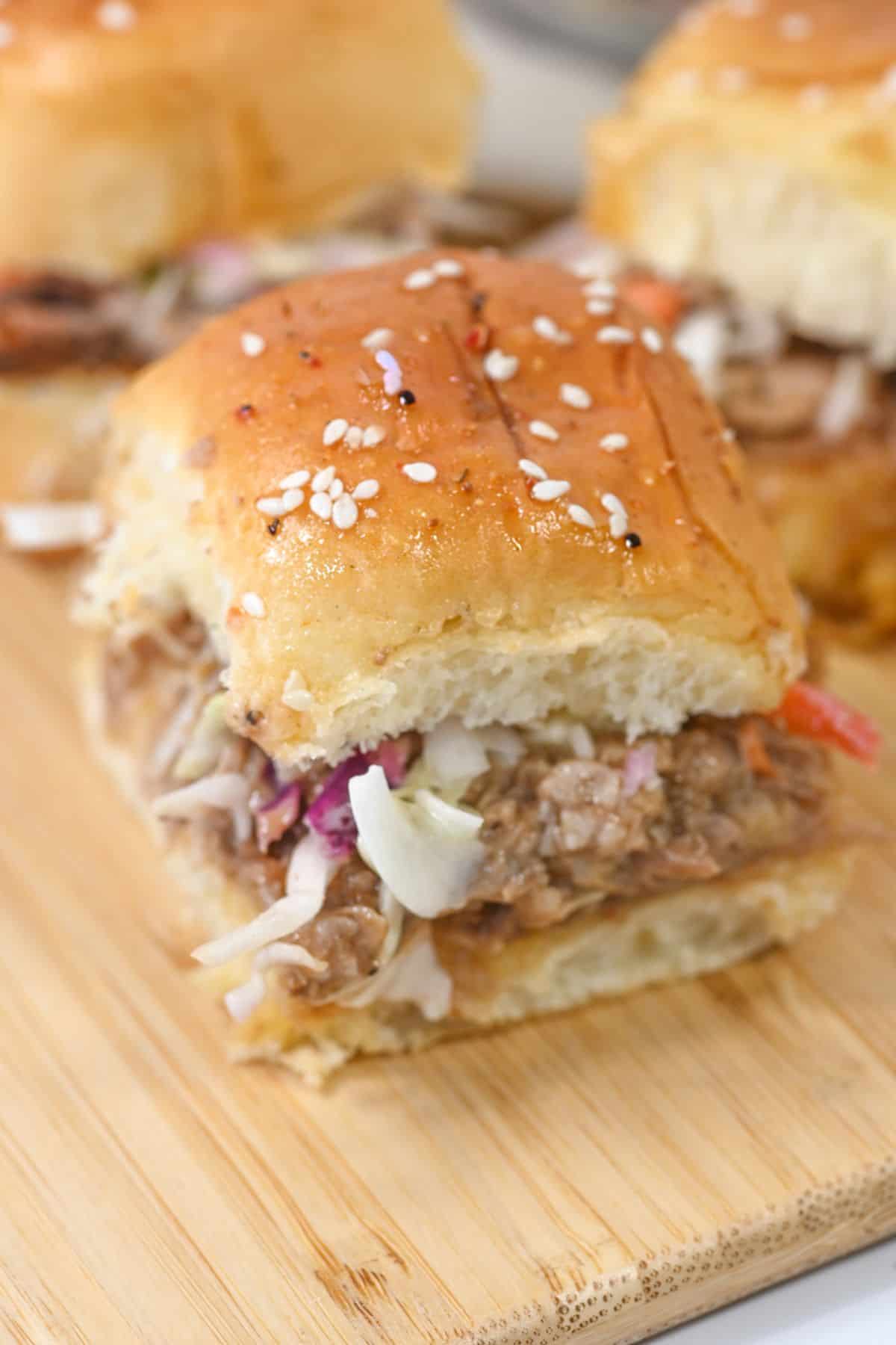 Close-up of delicious pork sliders featuring tender shredded pork topped with creamy coleslaw on a sesame seed bun, placed on a wooden board.