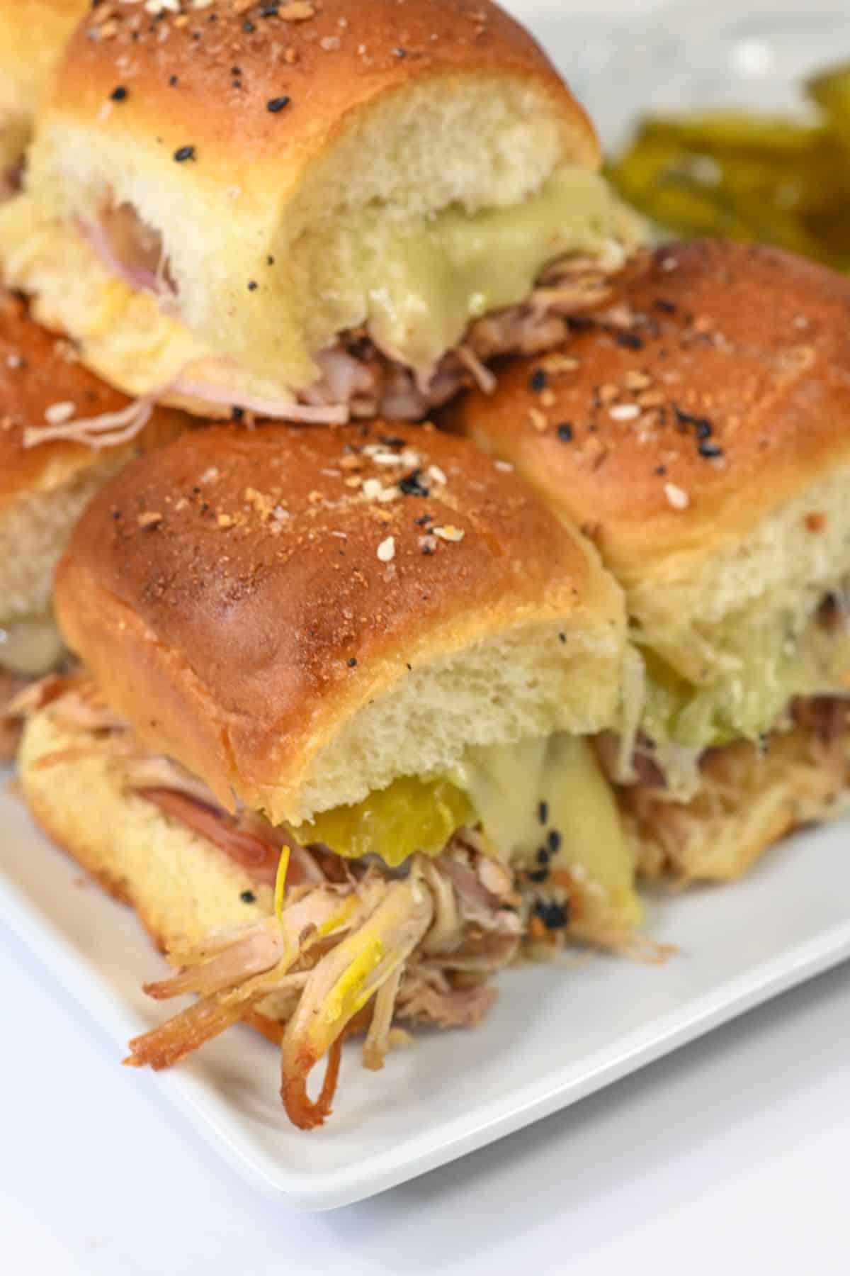 Three Cuban sliders with pulled pork, melted cheese, and pickles on a white plate, topped with a savory seasoning blend.
