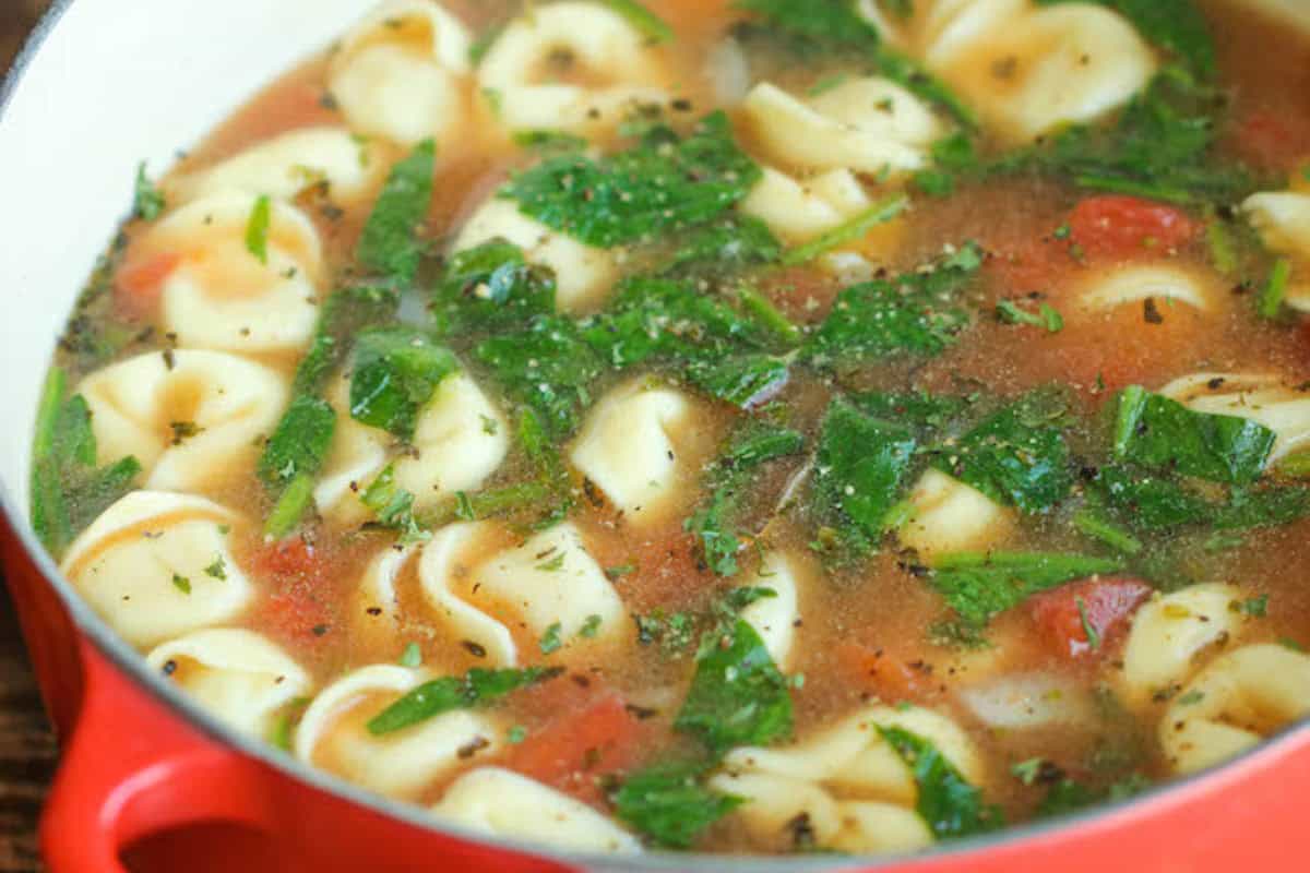 A pot of soup with cheese tortellini, spinach, chopped tomatoes, and herbs in a clear broth—perfect for fans of fresh tomato recipes.