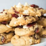 A plate of stacked white chocolate cranberry cookies rests on a white background, showcasing their delicious blend of flavors.
