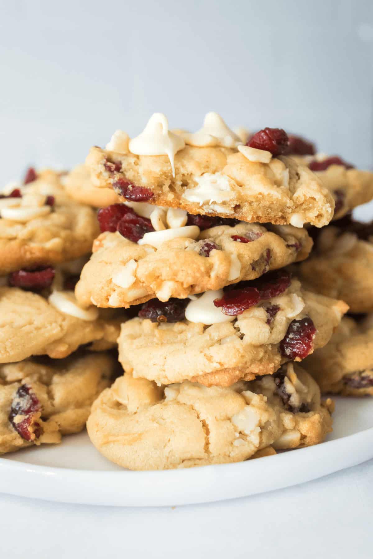 A plate of stacked white chocolate cranberry cookies rests on a white background, showcasing their delicious blend of flavors.