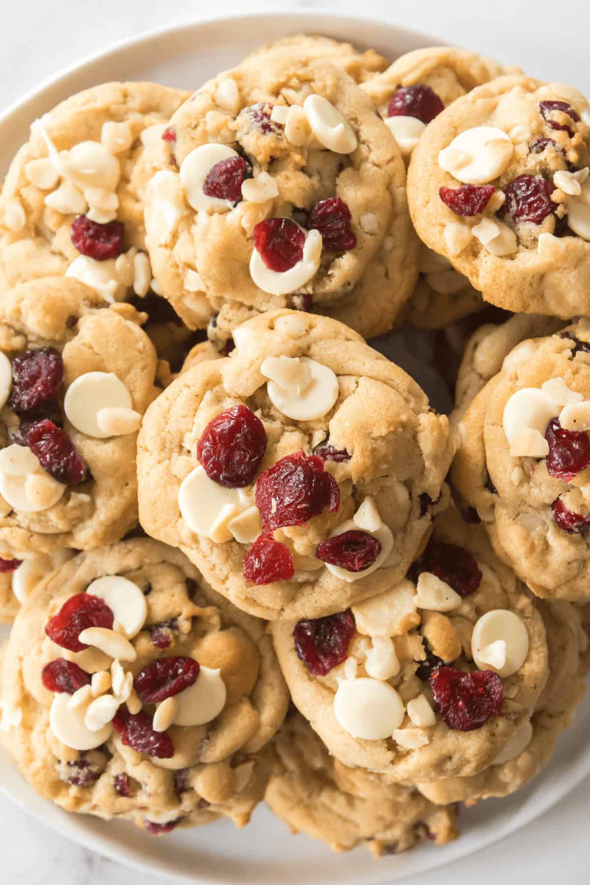 A plate of white chocolate cranberry cookies, topped with additional white chocolate chips and dried cranberries.