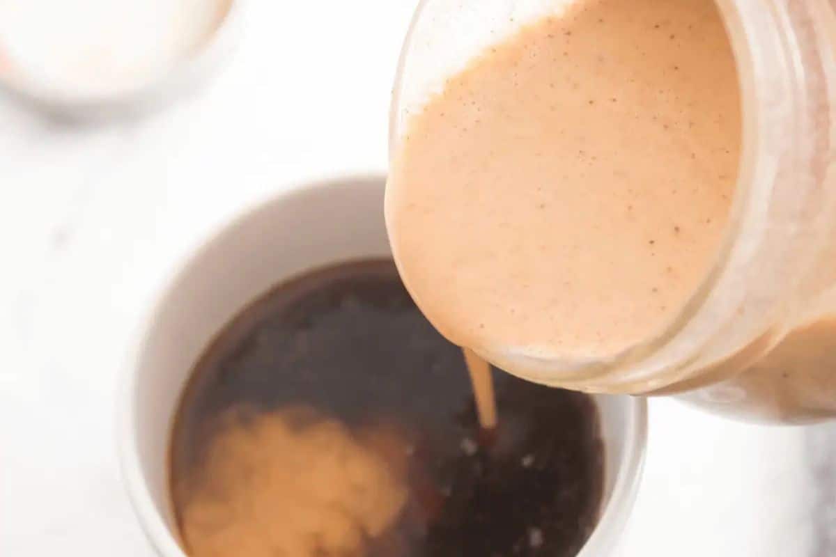 A jar of creamy pumpkin spice coffee creamer is being poured into a cup of black coffee.