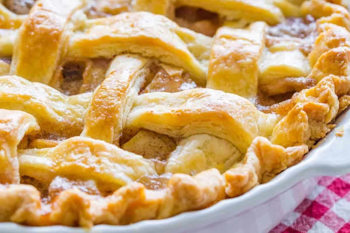 Close-up of a freshly baked, lattice-topped pie with a golden brown crust in a white dish, set on a red and white checkered tablecloth. This classic treat is reminiscent of old-fashioned dessert recipes passed down through generations.