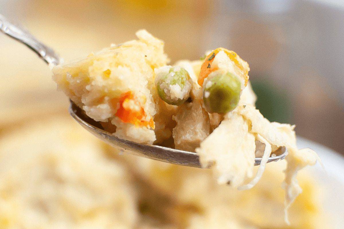 A close-up of a spoonful of food containing peas, carrots, and shredded chicken in a creamy sauce, reminiscent of Grandma's classic casserole recipes.