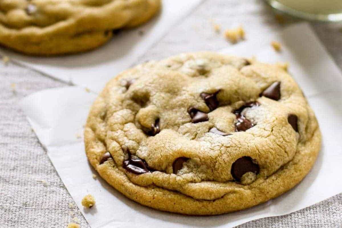 A close-up of a chocolate chip cookie resting on parchment paper, with another cookie partially visible in the background—a timeless treat that perfectly embodies old-fashioned desserts.