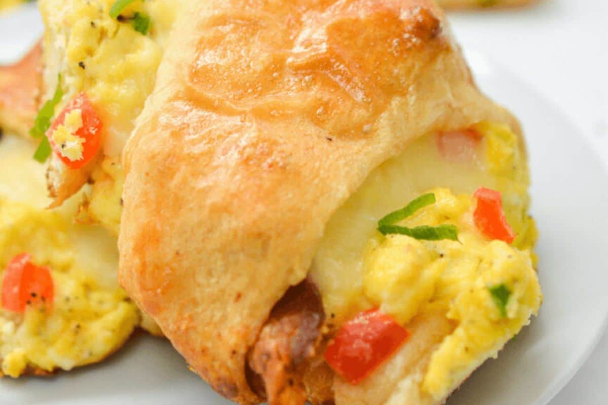 A close-up image of a piece of the crescent roll breakfast ring filled with scrambled eggs, diced tomatoes, green onions, and melted cheese.