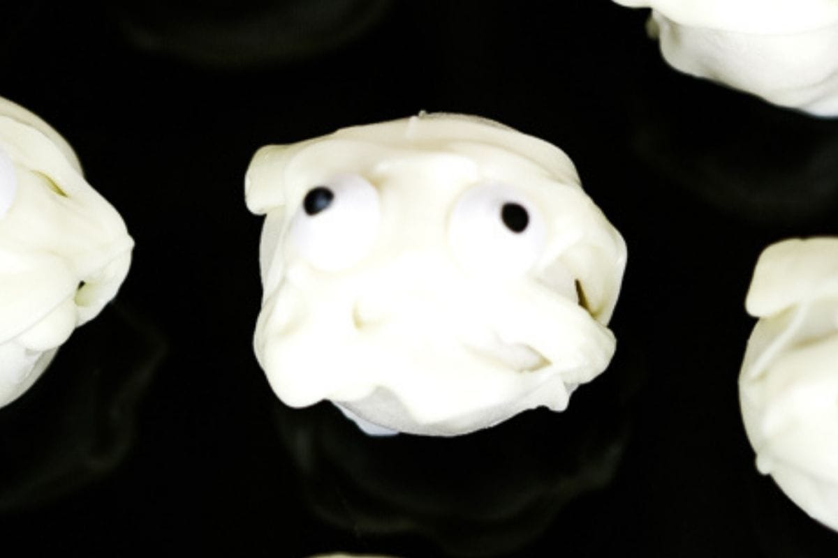A close-up of a small Halloween creature resembling a white dessert with googly eyes, set against a dark background.