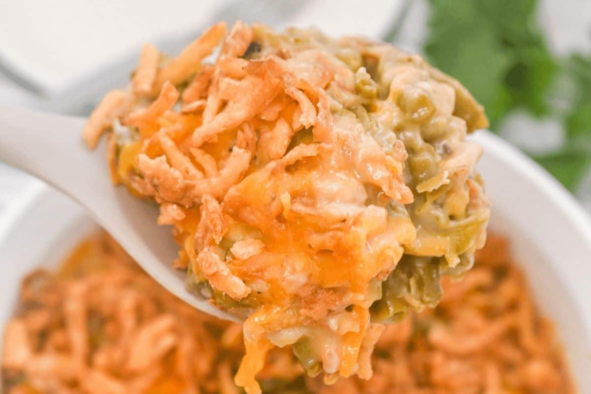 A close-up of a spoonful of green bean casserole topped with crispy fried onions, reminiscent of Grandma's vintage casserole recipes.