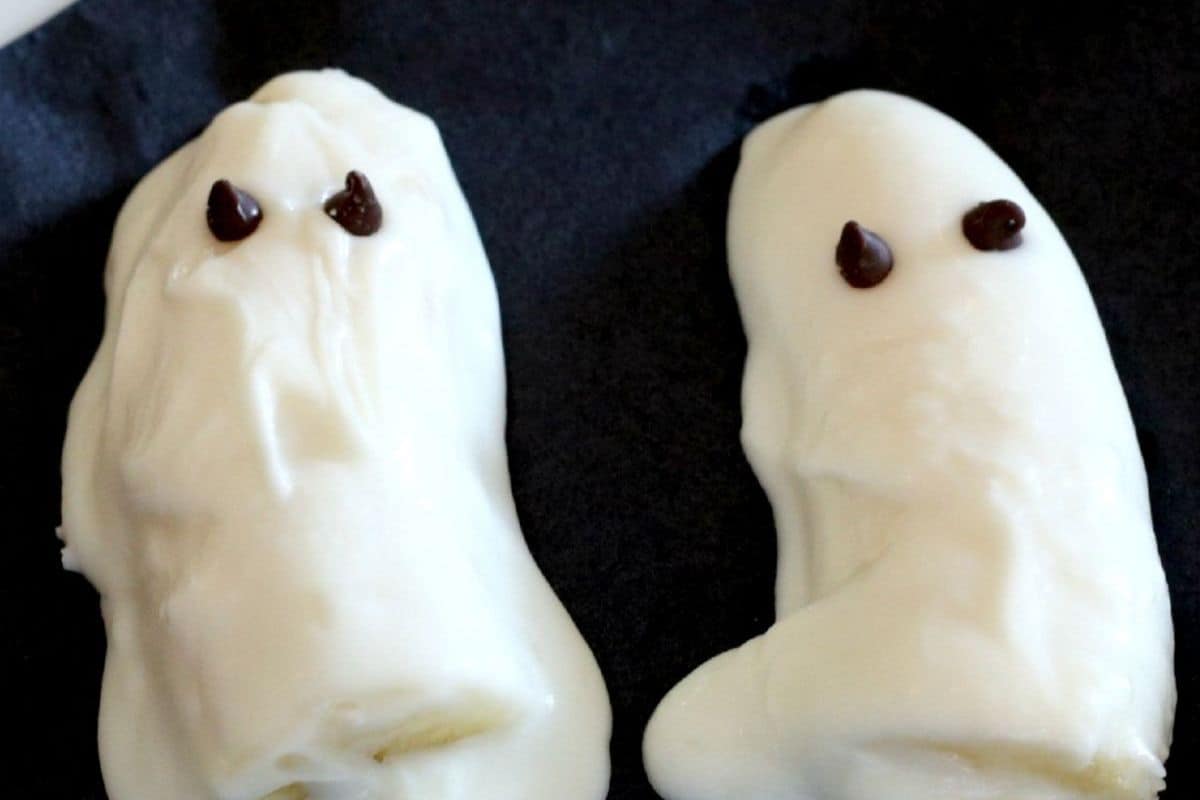 Two ghost-shaped treats covered in white chocolate with two small dark chocolate dots for eyes sit on a dark background, making for Real Scream Halloween Desserts.