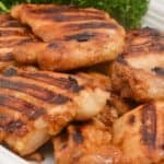Asian Grilled Chicken thighs with visible char marks are arranged on a white plate, garnished with a bunch of fresh parsley in the background.