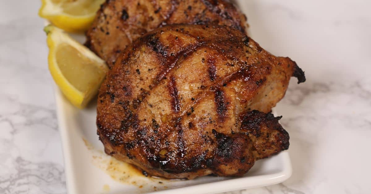 Grilled, seasoned boneless pork chops with char marks on a white plate, garnished with lemon wedges—perfectly mouthwatering and just as flavorful as any Grilled Pork Chops Marinade.