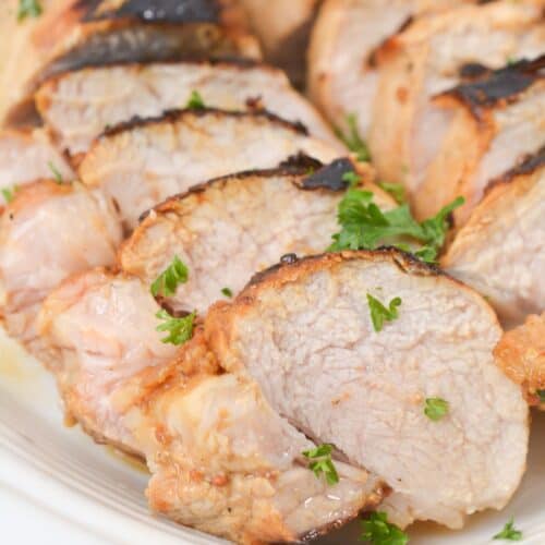 Sliced grilled marinated pork loin, garnished with chopped fresh parsley, served on a white plate.