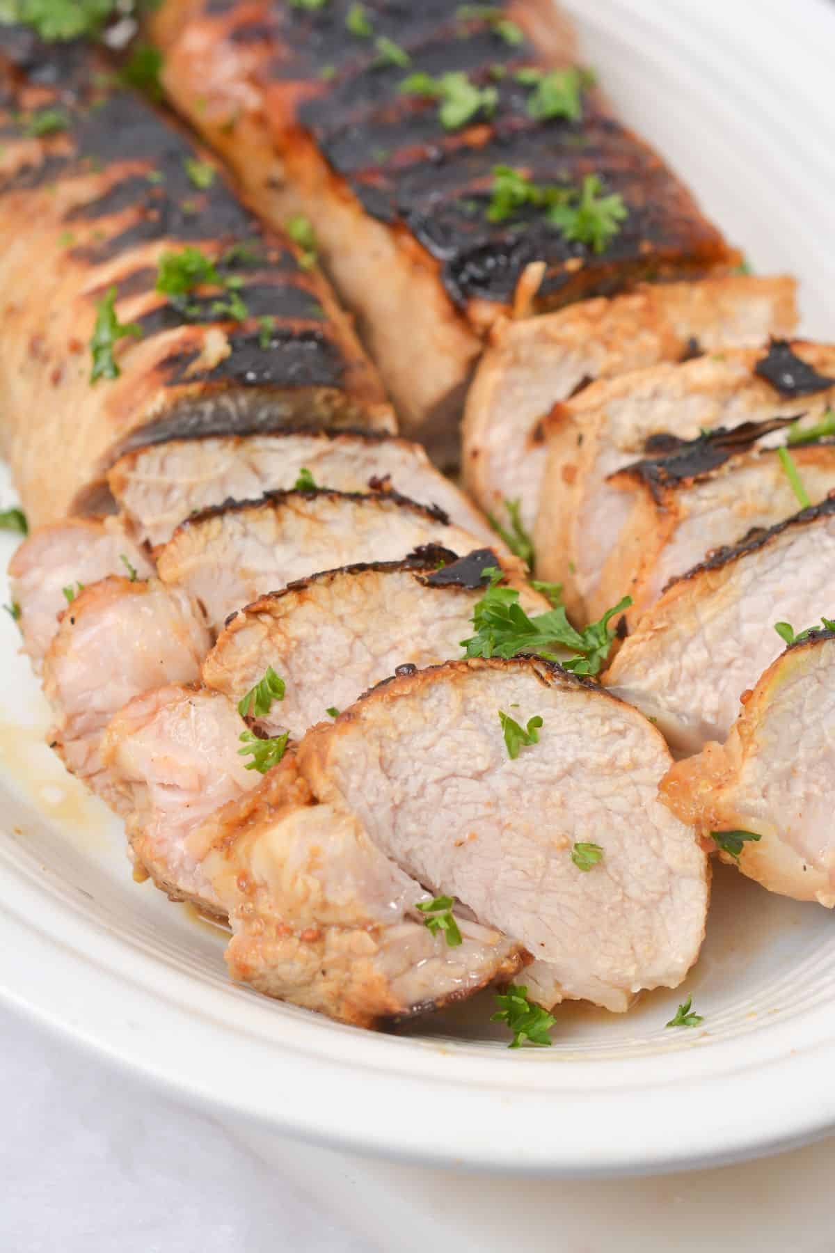 Sliced grilled marinated pork loin on a white plate, garnished with chopped parsley.