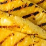 Several Grilled Pineapple Slices with visible grill marks are arranged on a green plate.