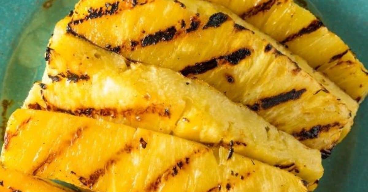 Several Grilled Pineapple Slices with visible grill marks are arranged on a green plate.