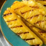 Fruit with char marks are artfully arranged on a turquoise plate, set atop a striped cloth.