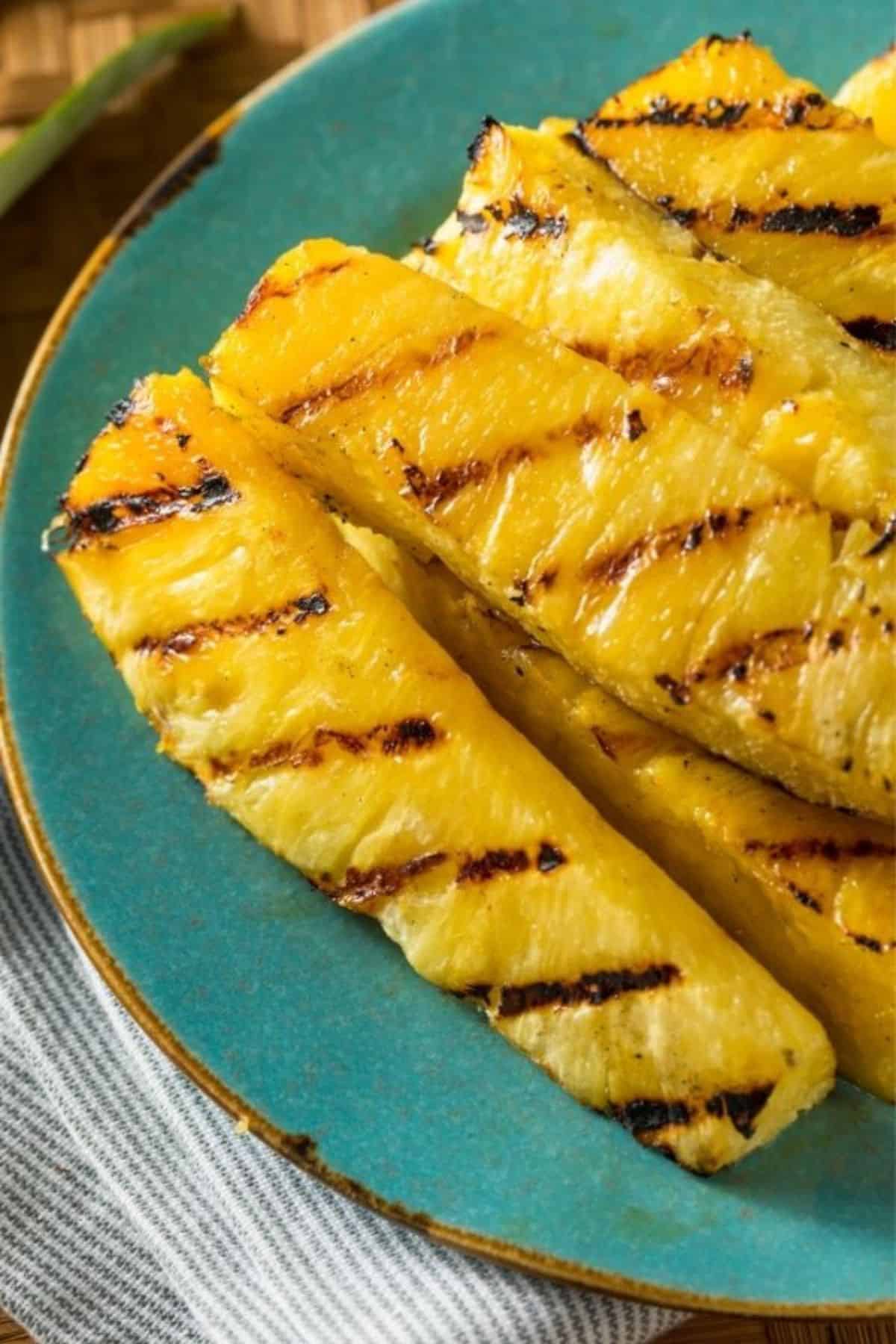 Fruit with char marks are artfully arranged on a turquoise plate, set atop a striped cloth.