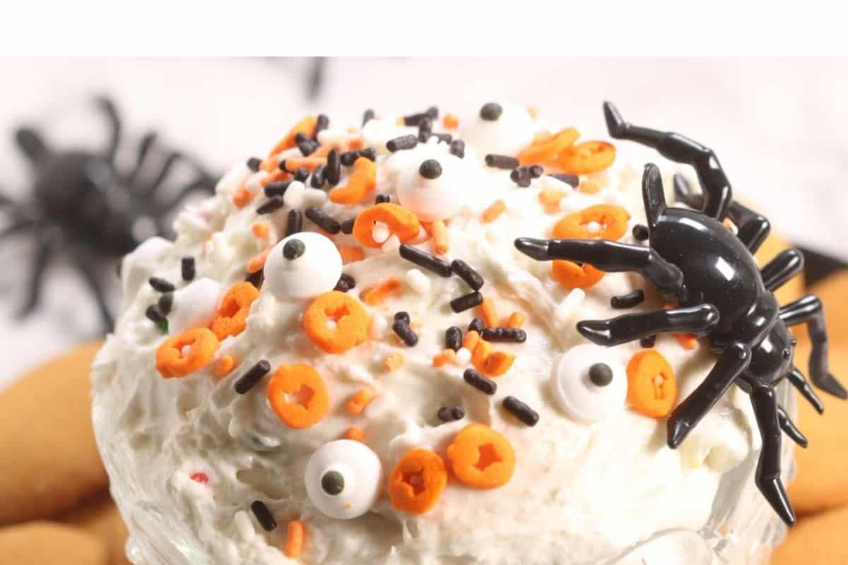 A scoop of white ice cream decorated with orange sprinkles, black sprinkles, candy eyeballs, and a black plastic spider makes for one of the spookiest Halloween desserts.