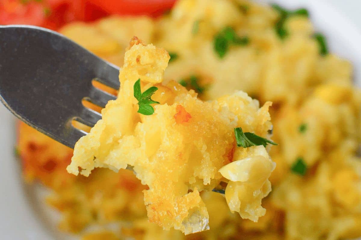 Close-up of a fork holding a bite of cheesy baked mac and cheese garnished with chopped parsley. The background shows the rest of the dish on a white plate, reminiscent of one of Grandma's vintage casserole recipes.