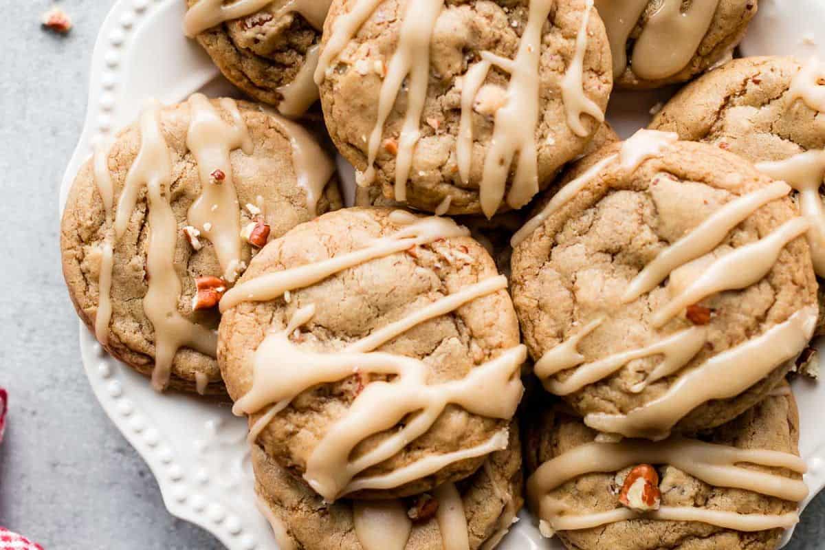 A white plate holding several timeless desserts, cookies drizzled with icing and containing small nut pieces.