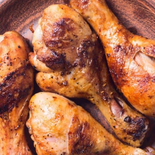 Four cooked, seasoned chicken drumsticks on a brown ceramic plate, each infused with a flavorful marinade for grilled chicken drumsticks.