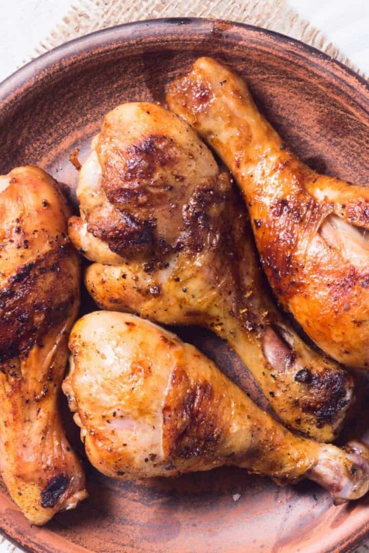 Four cooked, seasoned chicken drumsticks on a brown ceramic plate, each infused with a flavorful marinade for grilled chicken drumsticks.