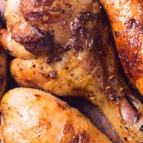 Four cooked, seasoned chicken drumsticks and thighs on a brown plate, showing crispy, golden-brown skin with visible grill marks—each piece bursting with flavor thanks to a savory marinade for grilled chicken drumsticks.
