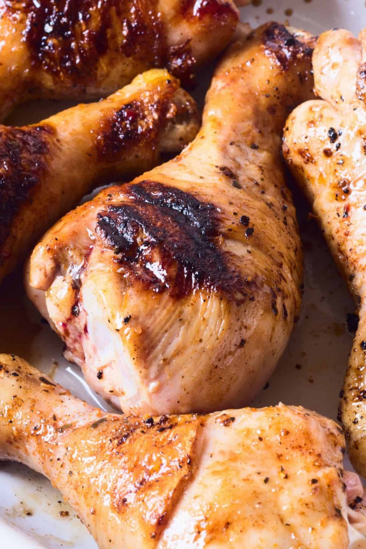 Close-up of several grilled chicken drumsticks with char marks and seasoning, arranged closely together on a white surface, showcasing the mouthwatering results of a flavorful marinade for grilled chicken drumsticks.