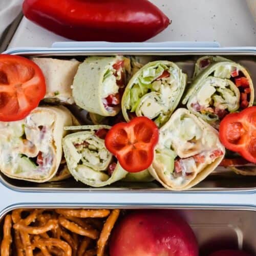 Discover kid-friendly lunchbox recipes with sliced tortilla wraps, fresh lettuce, and veggies, garnished with red bell pepper—served with pretzels and a peach for a fun, healthy way for kids to eat at school or on the go.