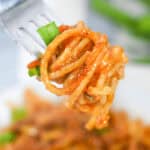 A fork holds a serving of the meal with adorned with zesty tomato sauce and vibrant green onions.