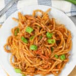A plate of Mexican spaghetti with meat sauce, infused with vibrant flavors and topped with chopped green onions, sits invitingly next to a fork and fresh green onions.
