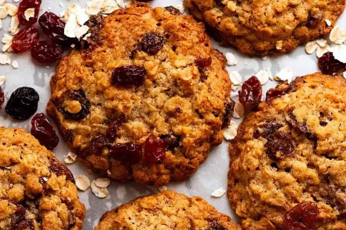 Close-up of old-fashioned oatmeal cookies with raisins and oats scattered around them on a light-colored surface. Perfect for those who cherish classic dessert recipes.
