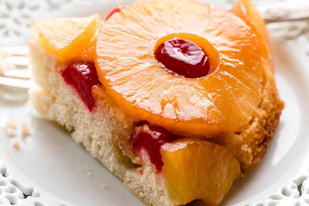 Close-up of a slice of pineapple upside-down cake, topped with caramelized pineapple slices and cherries, on a white decorative plate—a timeless favorite among classic desserts.