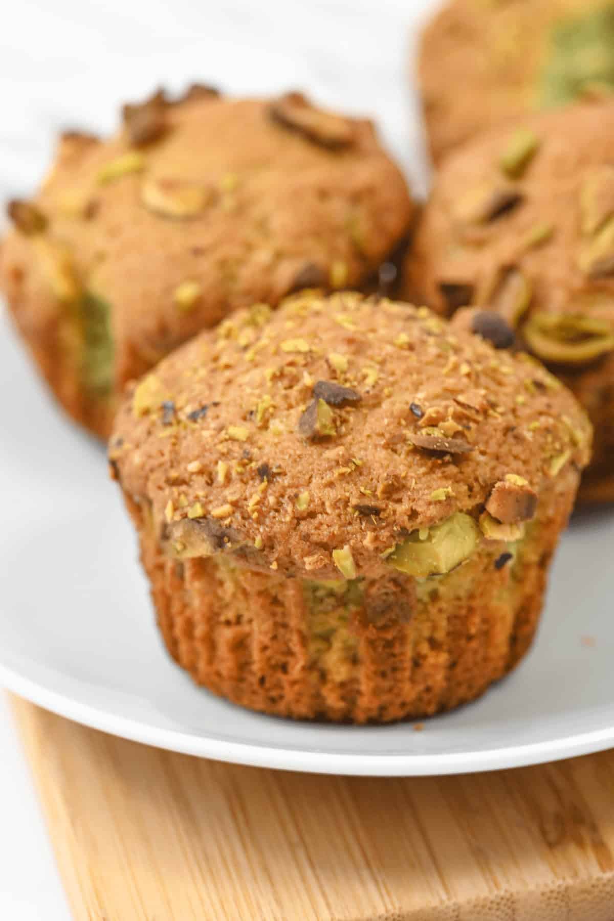 A close-up of pistachio muffins reveals their golden-brown tops with nut pieces prominently visible, showcasing their rich flavor.