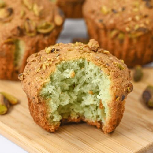 A close-up of delectable dessert on a rustic wooden board, with one muffin revealing a bite taken out and showcasing its enticing light green crumb within.