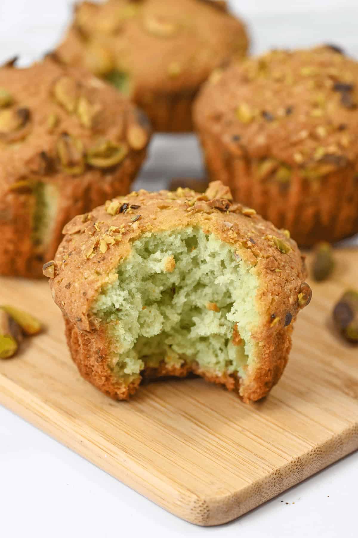 A close-up of delectable dessert on a rustic wooden board, with one muffin revealing a bite taken out and showcasing its enticing light green crumb within.