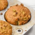 A close-up of freshly baked pistachio muffins nestles in a metal muffin tray, their golden tops enticing and aromatic, promising a delightful treat.