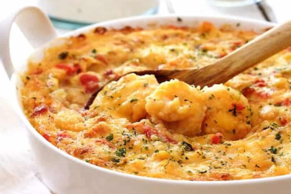 A wooden spoon scooping cheesy baked potato casserole garnished with herbs in a white dish showcases the essence of Grandma's recipes.