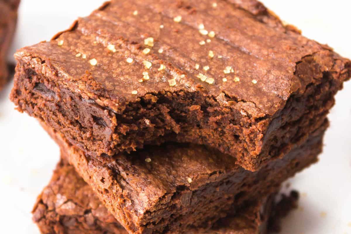 Close-up of two chocolate brownies stacked on top of each other, with a slightly crackled surface and a sprinkle of coarse sugar on top—a timeless dessert that brings classic desserts to life.