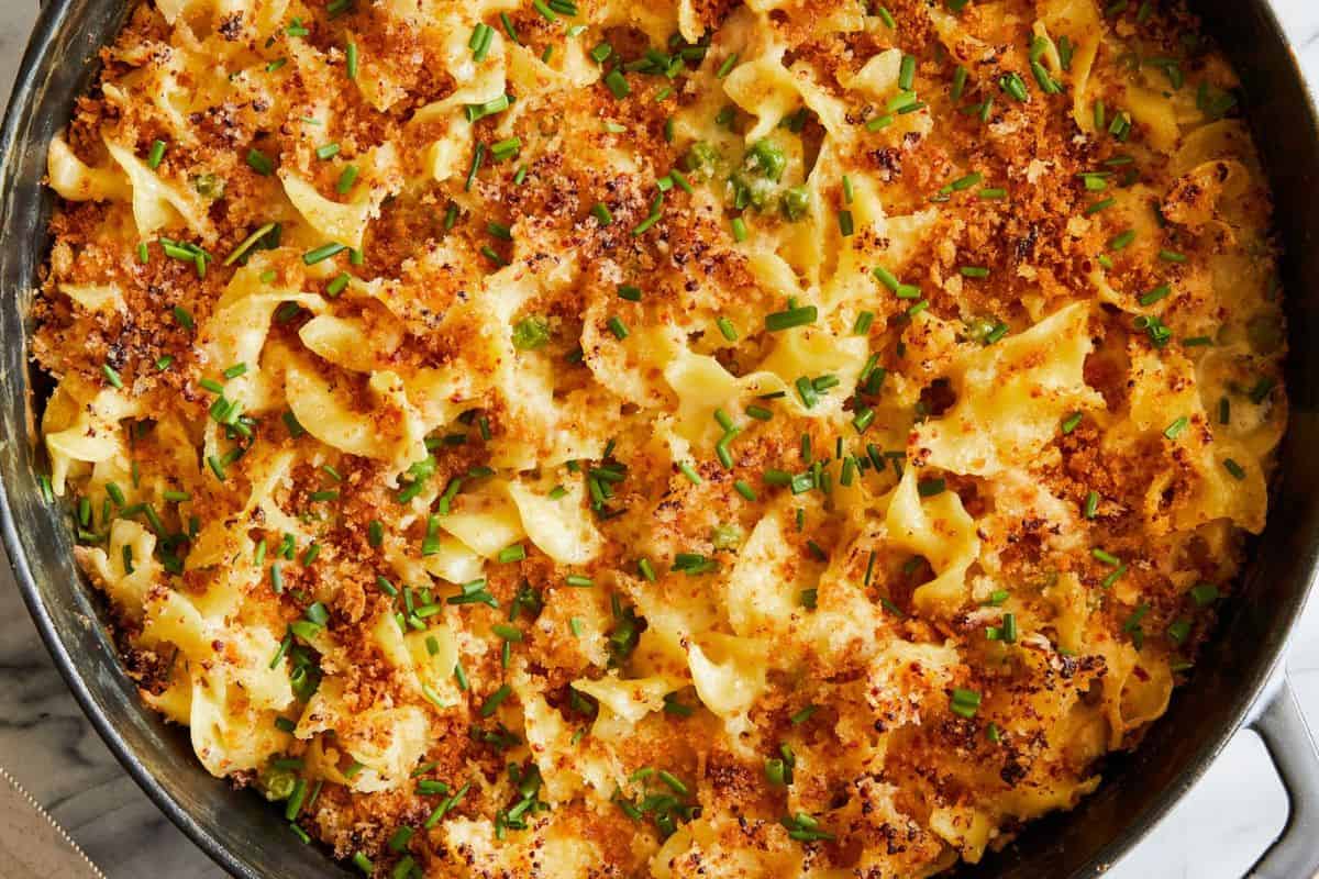 Close-up of a baked pasta dish topped with crispy breadcrumbs, melted cheese, and garnished with chopped chives in a dark baking dish, reminiscent of Grandma's vintage casserole recipes.