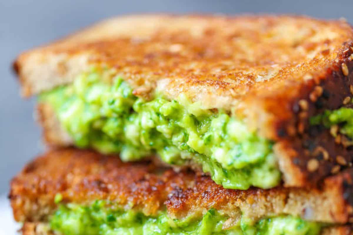 Close-up of a grilled cheese with a twist: sliced in half, revealing a creamy, green avocado mixture inside.