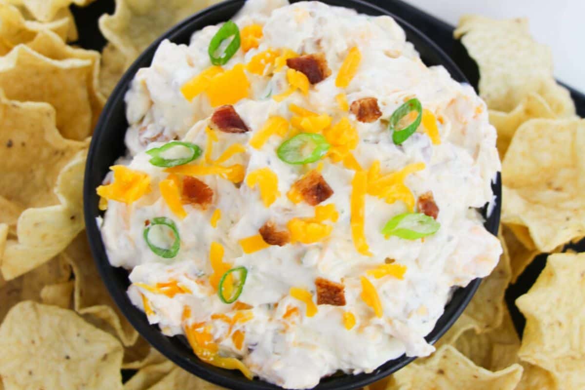 A bowl of bacon ranch cheddar dip surrounded by tortilla chips.