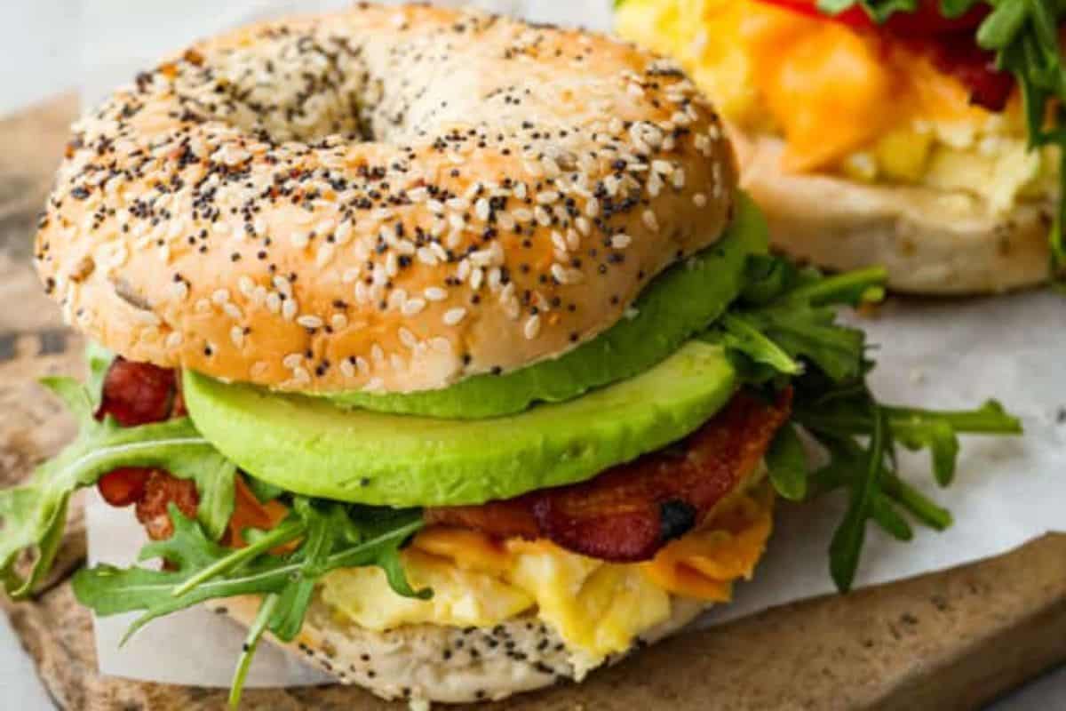 A closeup of a bagel Breakfast sandwich on a wooden cutting board.