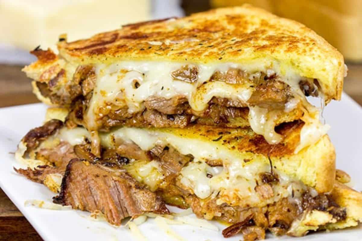 Grilled cheese with a twist, this sandwich is filled with gooey melted cheese and savory shredded meat, all stacked on a white plate.