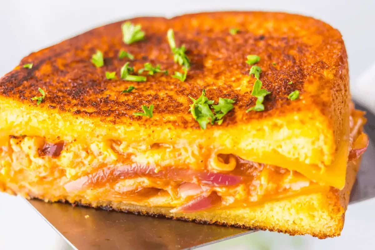 A close-up of a grilled cheese with a twist features crispy bread, molten cheese, and savory onions, all garnished with fresh chopped herbs.