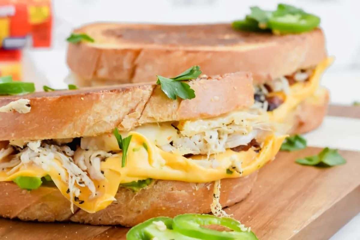 Grilled cheese with a twist: sandwiches featuring shredded chicken and jalapeños, all artfully presented on a wooden board and garnished with parsley.