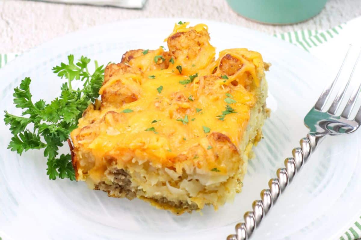 A serving of Tater Tot Sausage Breakfast Casserole on a white dish with a silver fork.