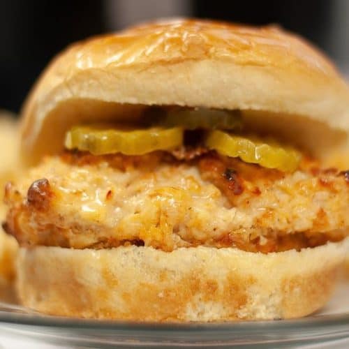 A copycat Chick-fil-A sandwich with pickles on a bun, served with a side of crinkle-cut fries.