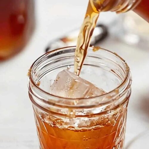 A brown liquid is being poured into a glass filled with ice cubes, creating the perfect Game Day Cocktail for your next celebration.
